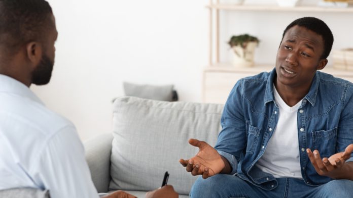 Two men sitting on a couch and speaking with each other