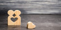 Two wooden figures hugging, with a heart-shaped cutout removed between them both