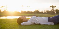 A relaxed woman laying in the grass as the sun rises