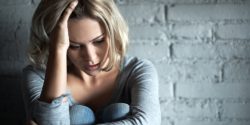 A distraught looking woman sitting against a white brick wall