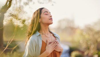 A woman with her hands on her chest, eyes closed, breathing in fresh air
