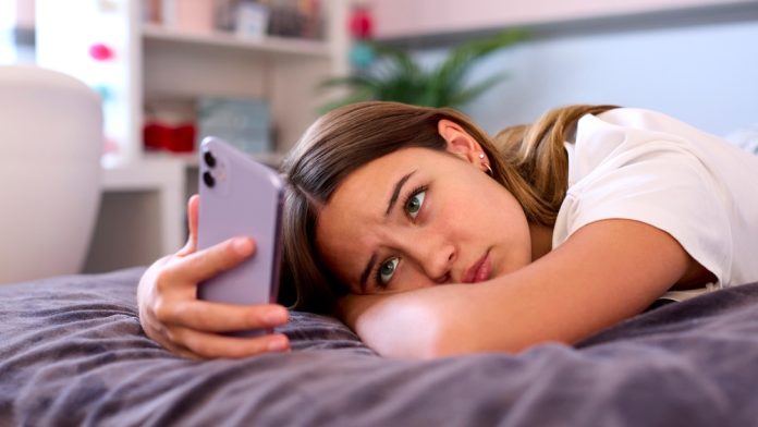 A depressed looking teen looking at their phone in bed