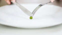 a person using a fork and knife to cut a pea, signifying an eating disorder