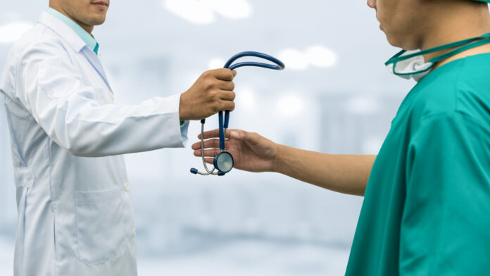 A doctor hands a stethoscope to a surgeon