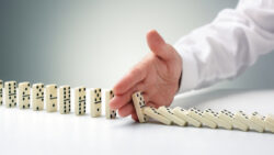 A hand blocks a line of falling dominoes, signifying someone staging an intervention