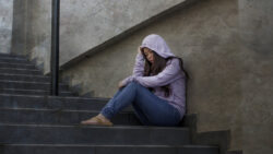 A sad woman in a hoodie sits on some concrete stairs